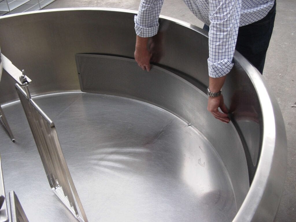 Person adjusting a large stainless steel industrial mixer bowl.