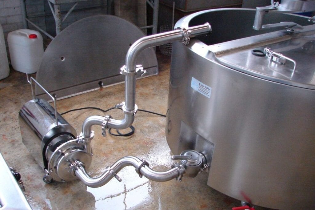 Industrial stainless steel piping connected to a tank in a facility.