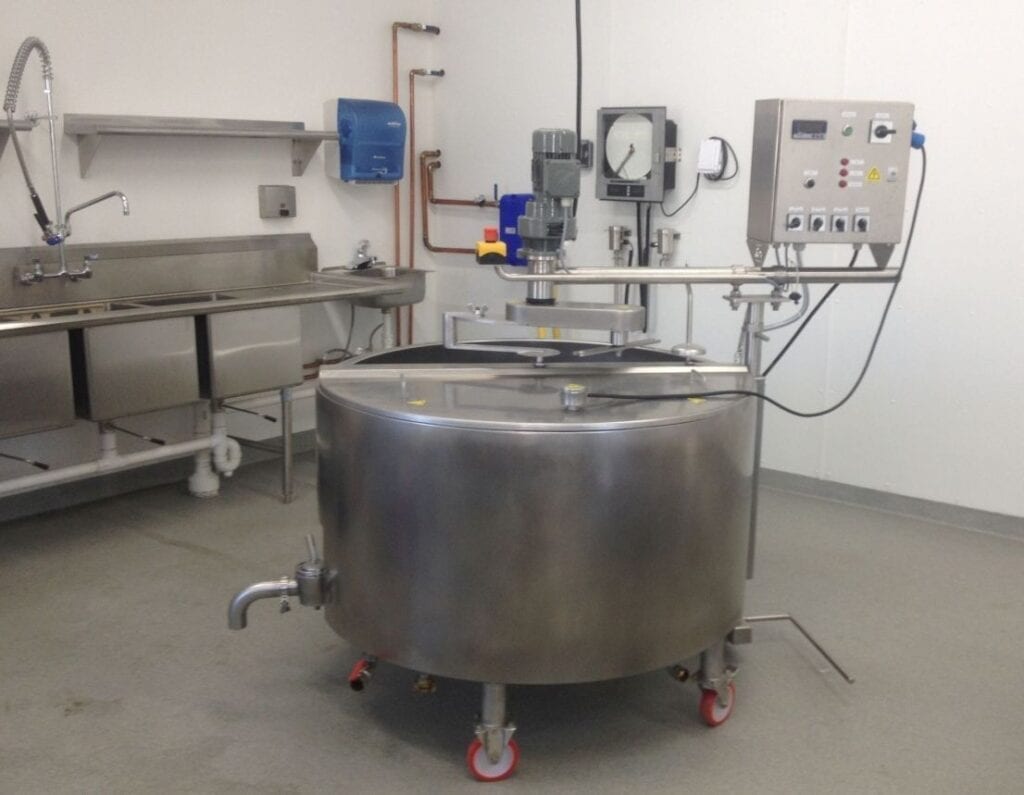 Large stainless steel mixing tank with control panel in a clean industrial kitchen or processing room.