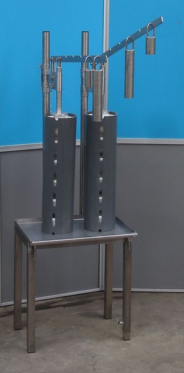 Two metallic structures with holes, standing on a metal table against a blue background.