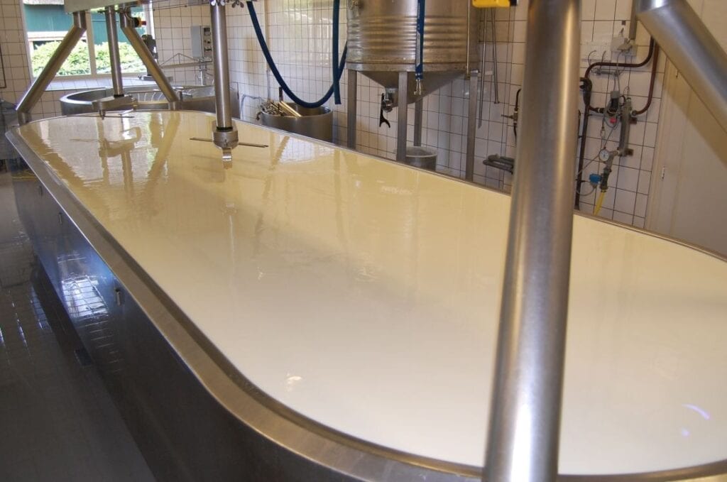 Long white sink with multiple faucets in a tiled room.