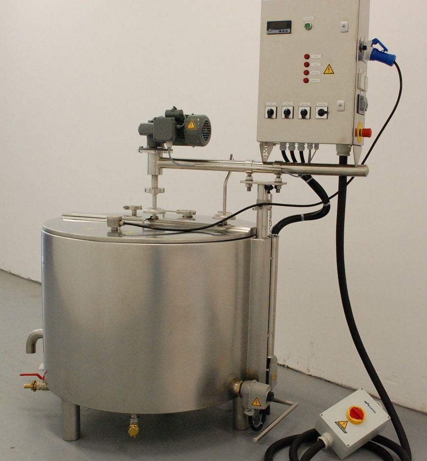 A stainless steel industrial mixing tank with attached control panel, mixer motor, pipes, and emergency stop button, positioned in a plain room.