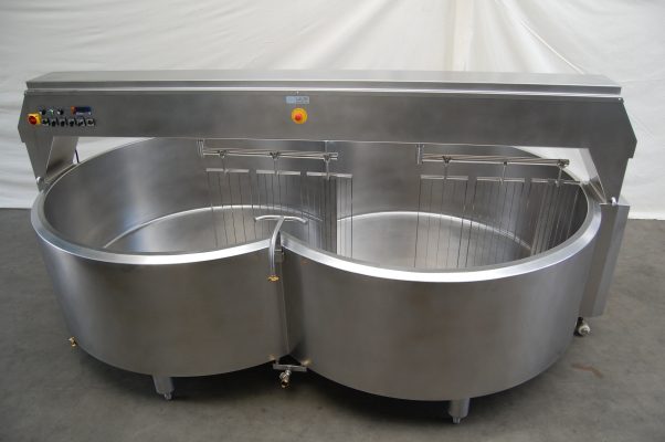 Large stainless steel industrial cheese vat with two connected round compartments and control panel, placed on a concrete floor with a white background.